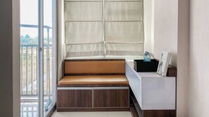 Un balcon avec un banc rembourré, une petite table avec une bouteille d’eau et une vue sur la verdure environnante.