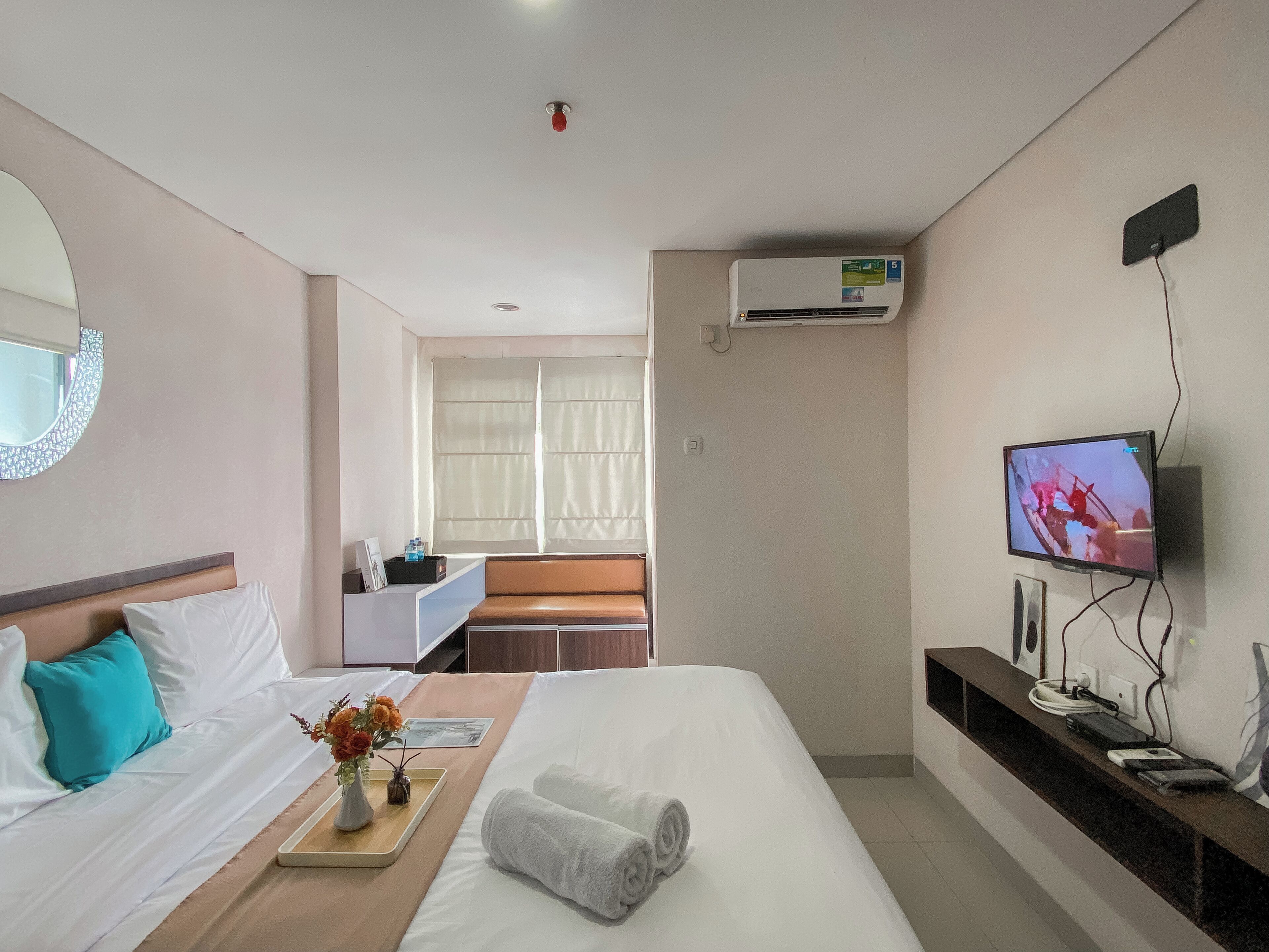A hotel room with a bed, a desk, a television, and an air conditioning unit.