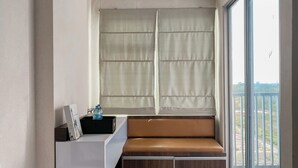 A balcony with a cushioned bench, a small table with a water bottle, and a view of the outdoors.