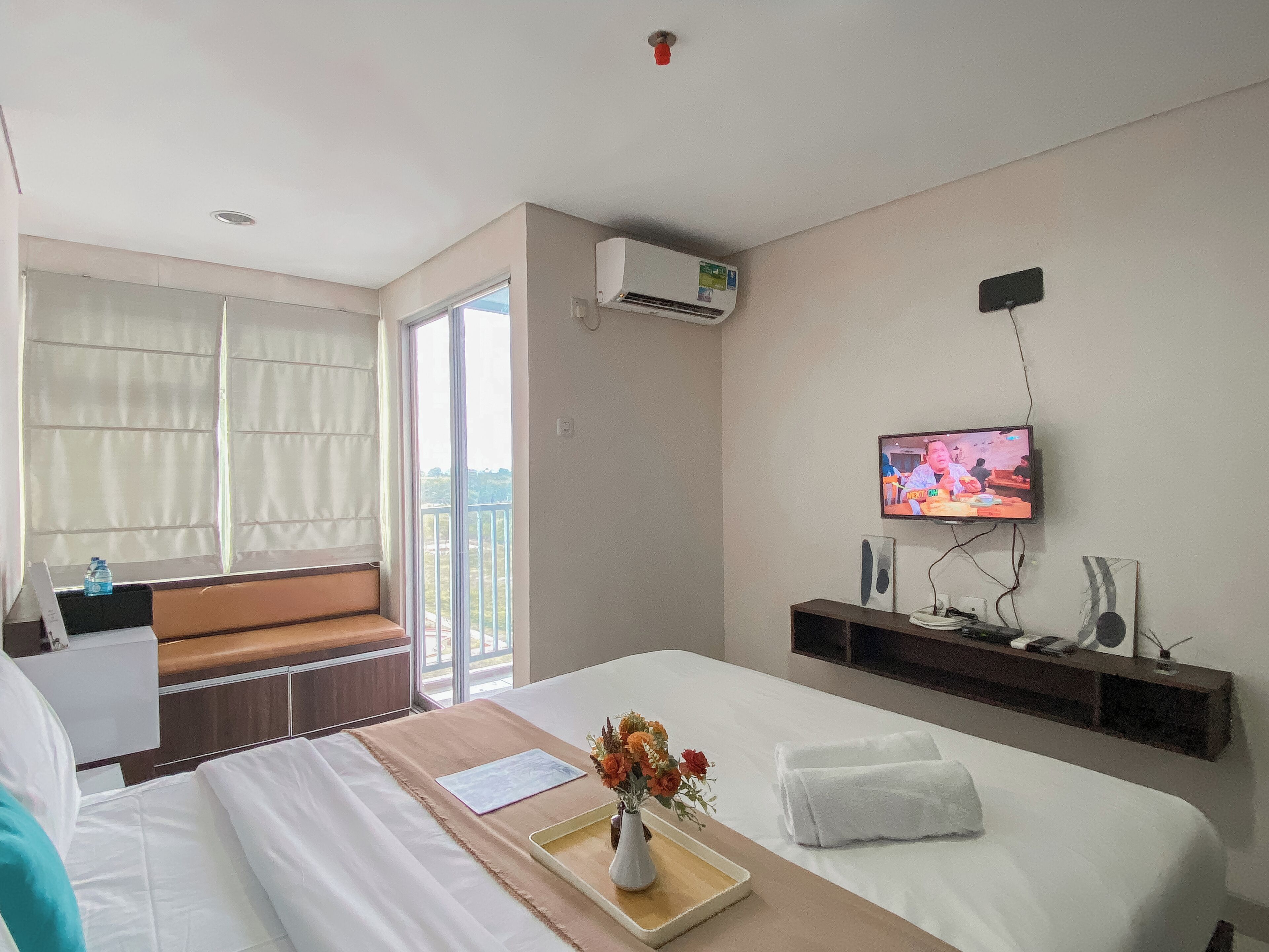 A hotel room with a bed, a TV, a balcony, and a small table with a vase of flowers.