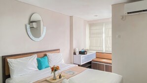A hotel room with a bed, a bedside table, a mirror, a vanity with a mirror, and a window with curtains.