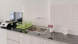 A kitchen with a stainless steel sink, a green dish rack, and a white vase with flowers.