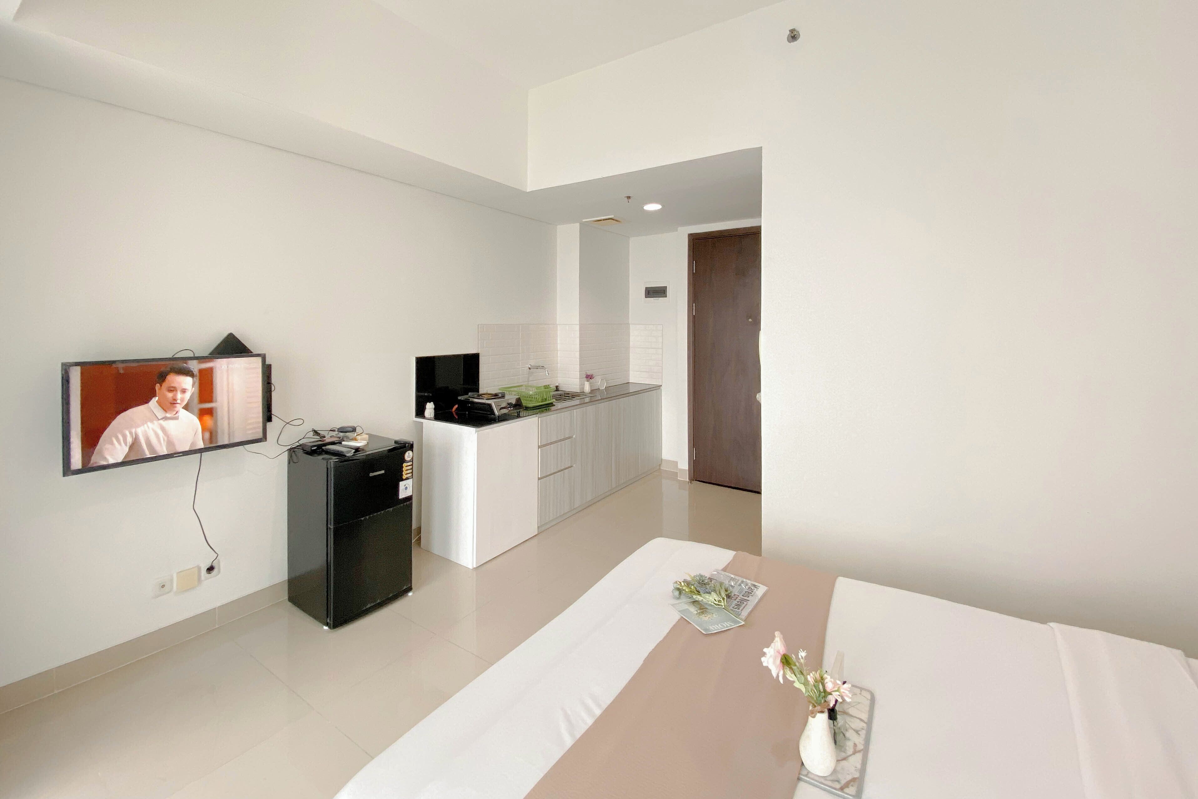 Quarto de hotel moderno com televisão, pequeno espaço de cozinha, área de refeições e porta que dá para outro cômodo.