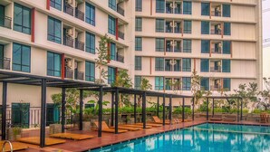 A swimming pool with lounge chairs and a covered seating area, surrounded by a multi-story building with balconies.