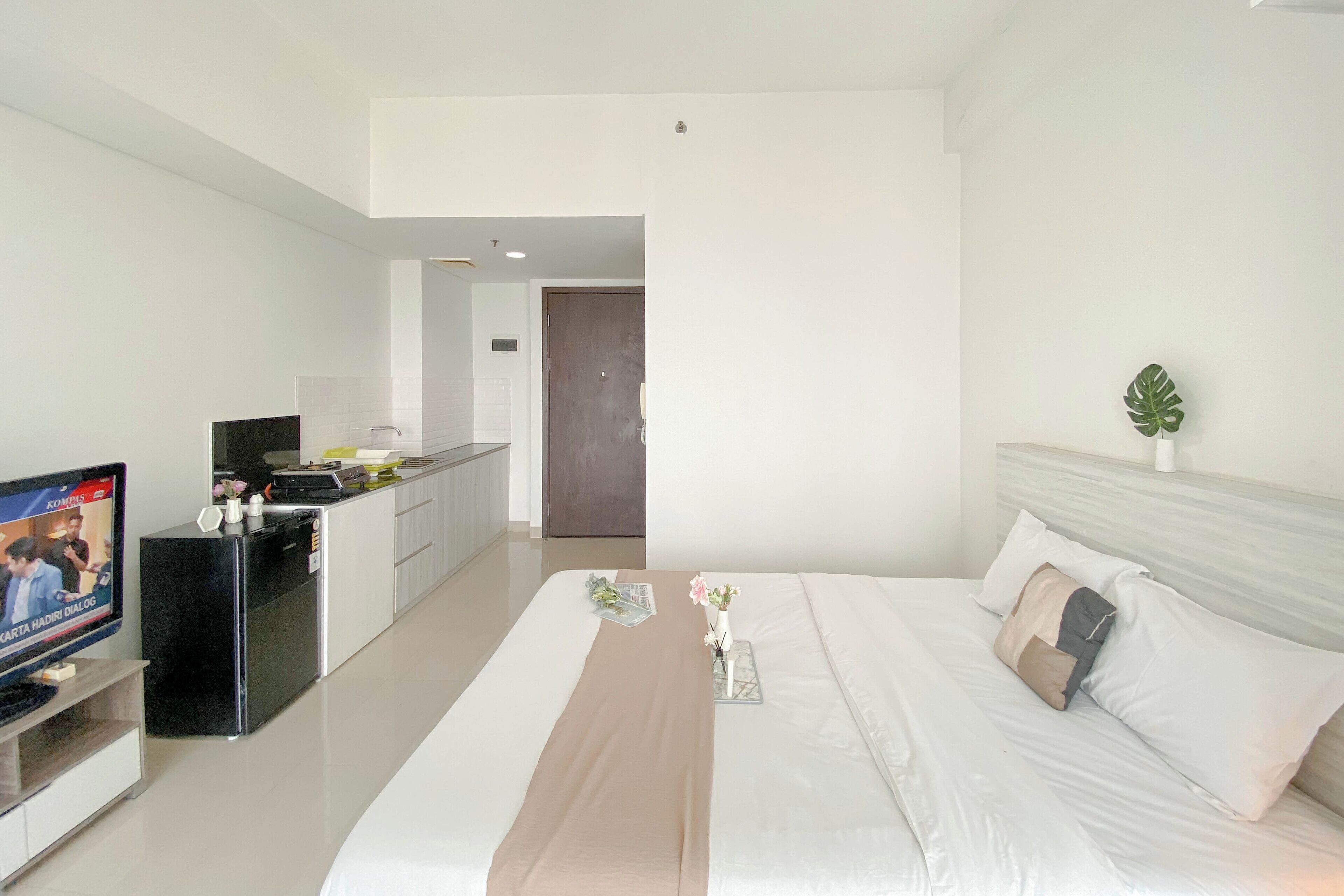 Ein Hotelzimmer mit einem Bett, einem Fernseher, einer kleinen Küchenzeile und einer Tür zu einem weiteren Raum.