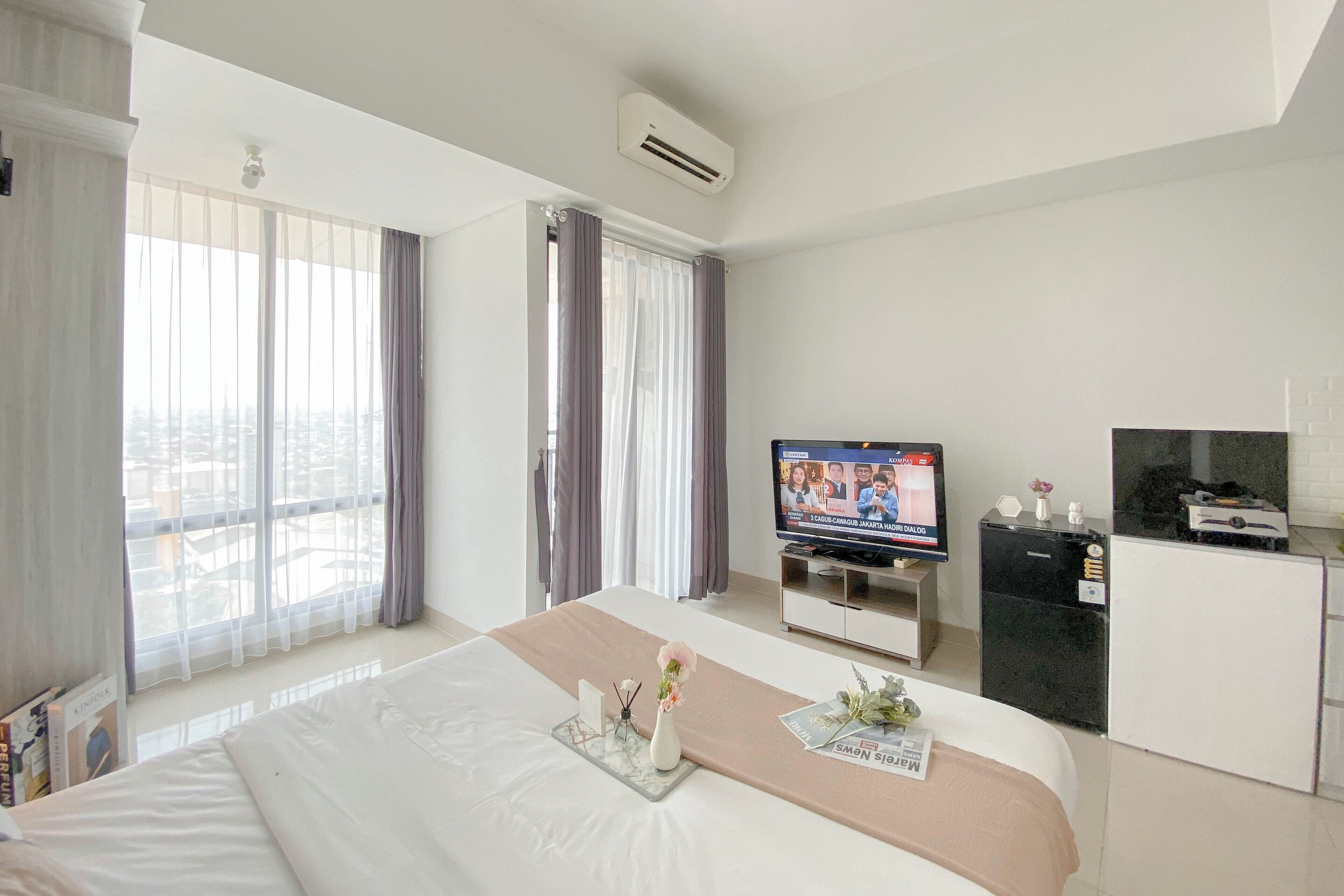 A hotel room with a bed, a TV, a minibar, and a window with curtains.