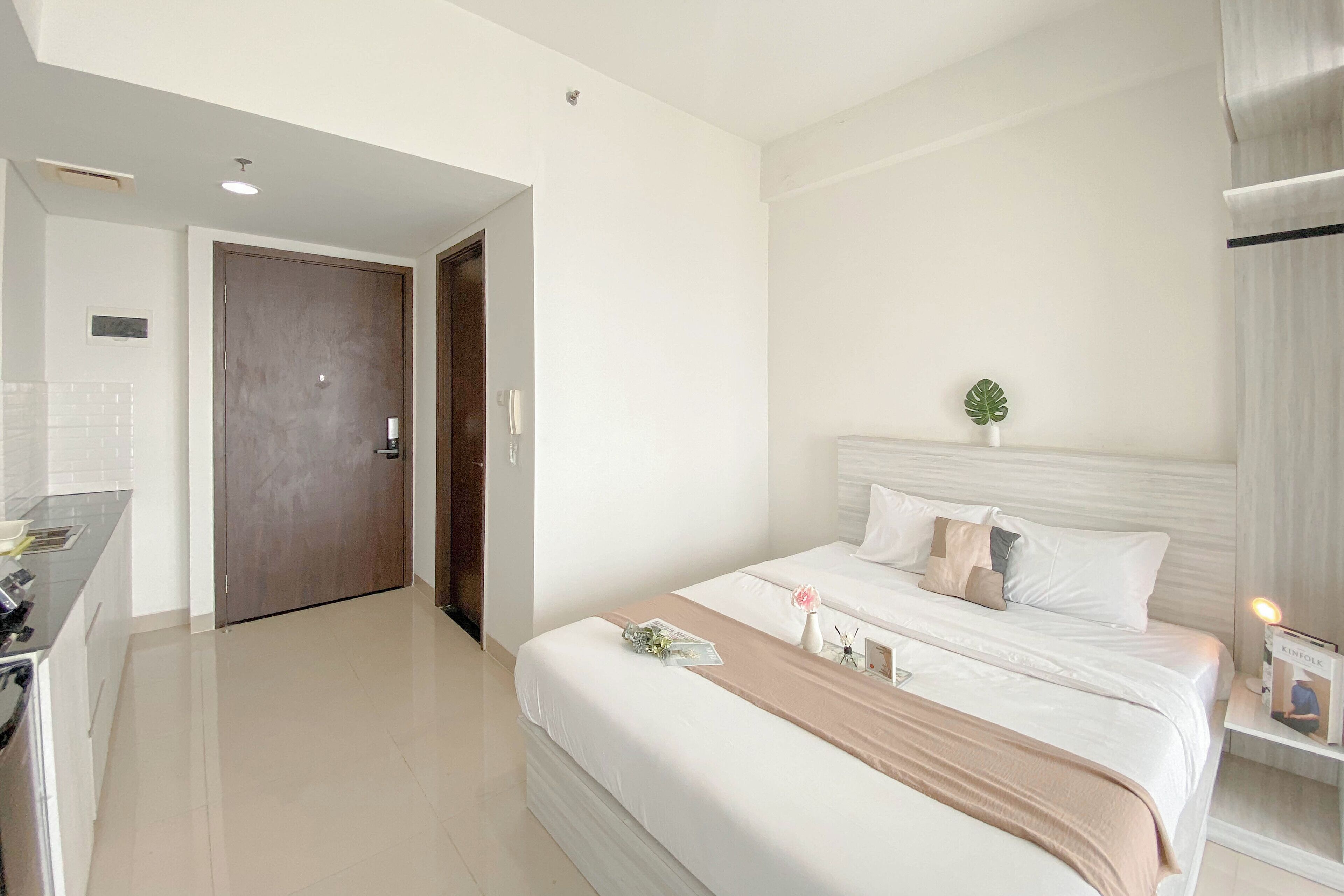 A hotel room with a bed, bedside table, and a small plant.
