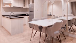 A modern kitchen with a central island, a dining area with a white table and grey chairs, and a large mirror reflecting the space.
