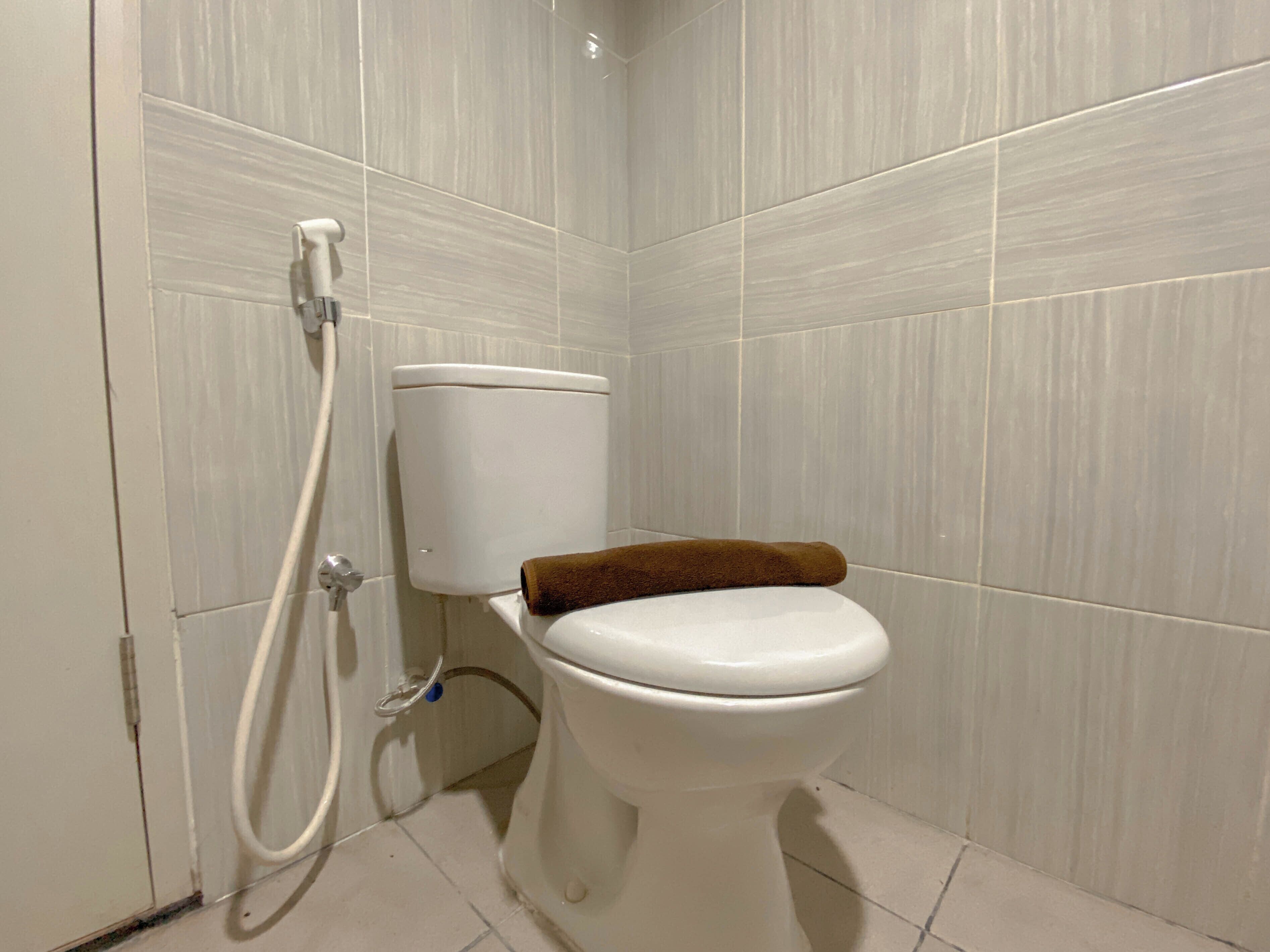 Ein Badezimmer mit Toilette, Duschschlauch und einem Handtuch auf dem Sitz.