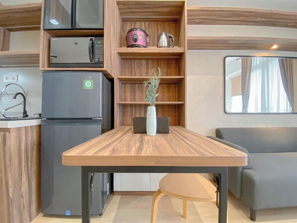Une cuisine compacte équipée d’un four à micro-ondes, d’un réfrigérateur et d’une machine à café, le tout placé sur une étagère. On y trouve également une petite table avec un vase de plantes et un banc.