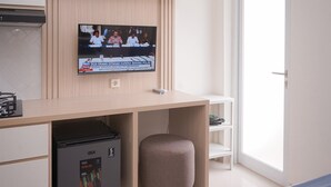 A modern hotel room with a wooden desk, a television mounted on the wall, a GE appliance, and a small stool.