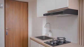 A compact kitchen with a wooden door, a stainless steel sink, a gas stove, and a modern range hood.