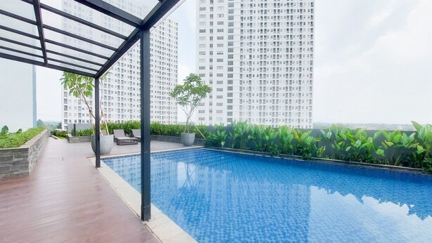A rooftop swimming pool with a tiled floor, surrounded by greenery and a view of tall buildings.