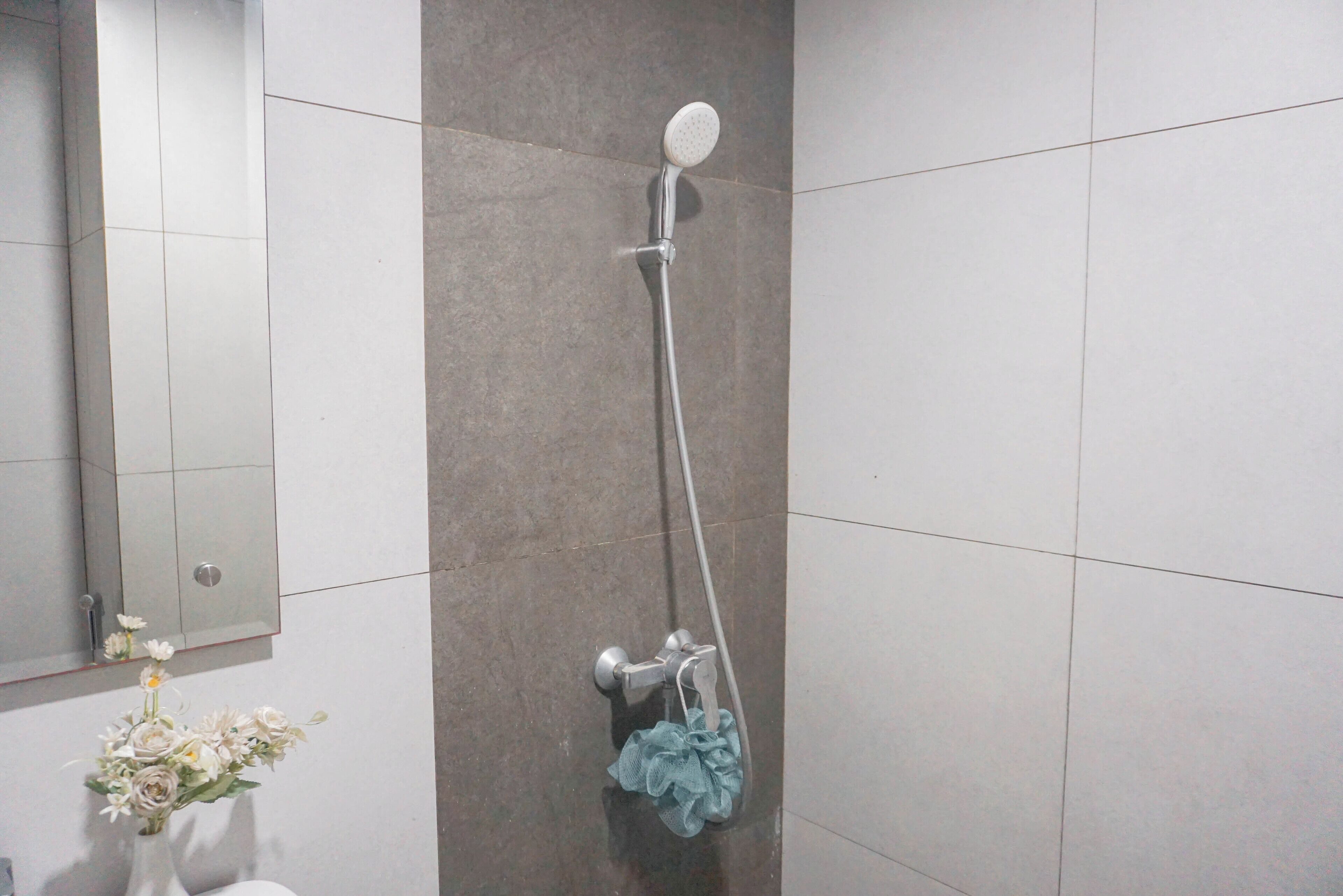 Ein Badezimmer mit Dusche, Spiegel und einer Blumenvase.