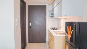 A compact kitchen with a dark wooden door, a black refrigerator, and a sink. - Cozy Look Studio Apartment At Lrt City Bekasi (Bekasi)