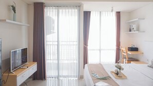 A hotel room with a bed, bedside table, TV, and curtains. - Cozy Look Studio Apartment At Lrt City Bekasi (Bekasi)
