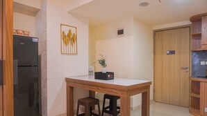 A compact kitchen with a refrigerator, wooden table, two stools, a vase with flowers, and a wooden cabinet. - Spacious 3Br Apartment At Meikarta (Cikarang)