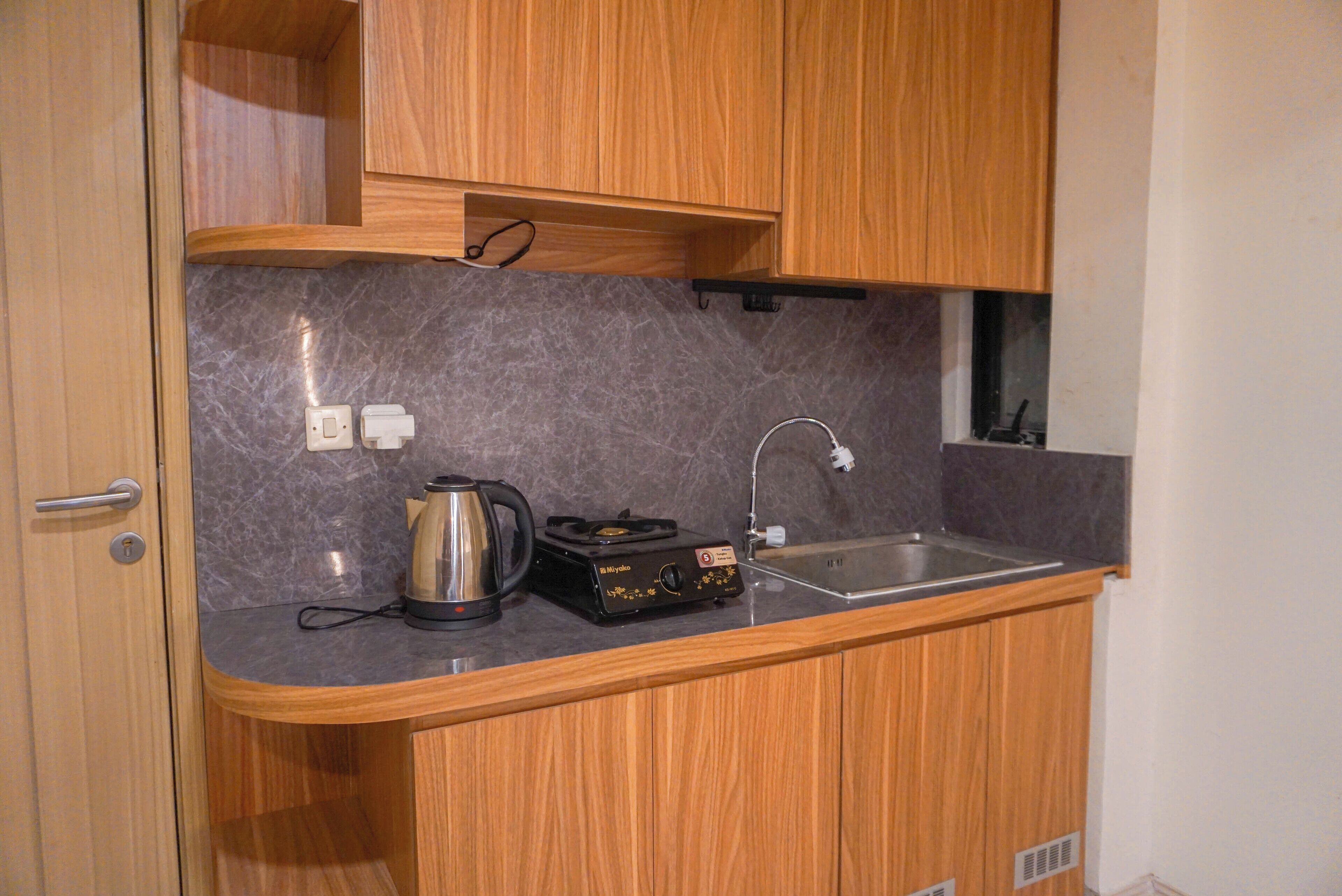 A compact kitchen with wooden cabinets, a marble countertop, a kettle, a portable stove, and a sink.
