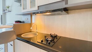 A modern kitchen with a gas stove, stainless steel sink, and white cabinets. - Homey And Modern 2Br At Patraland Urbano Apartment (Bekasi)