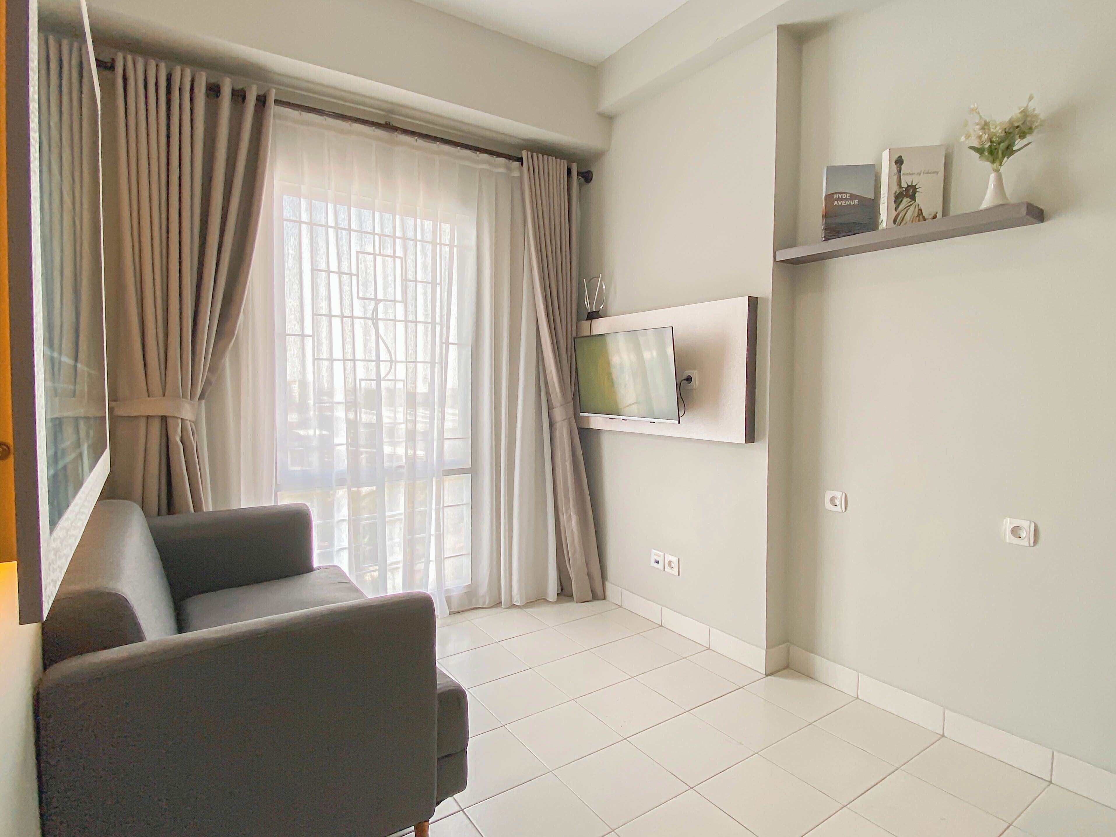 A modern living room with a sofa, a TV mounted on the wall, and a window with curtains.