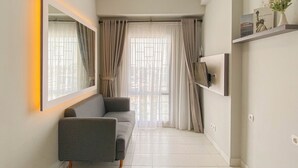 A modern living room with a grey sofa, a large mirror, and a TV mounted on the wall. - Homey And Modern 2Br At Patraland Urbano Apartment (Bekasi)