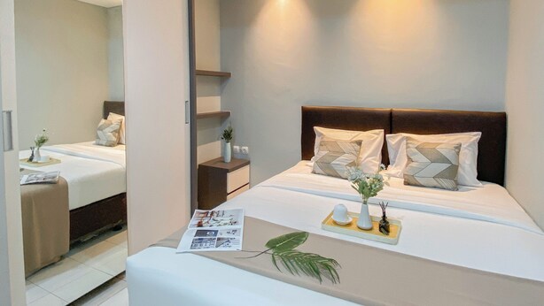 A modern hotel room with a large bed, bedside tables, and a mirror. - Homey And Modern 2Br At Patraland Urbano Apartment (Bekasi)