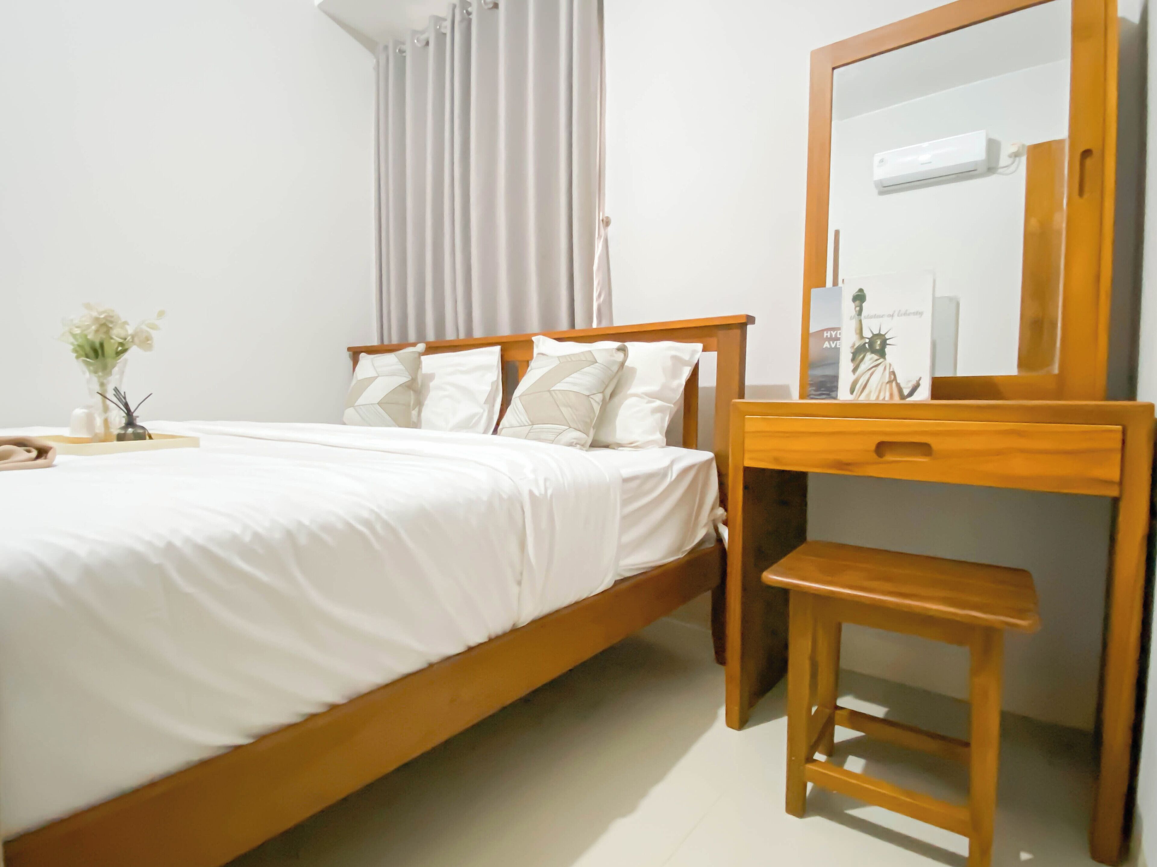 Un dormitorio con una cama de madera, una mesita de noche con lámpara, un espejo y una ventana con cortinas.