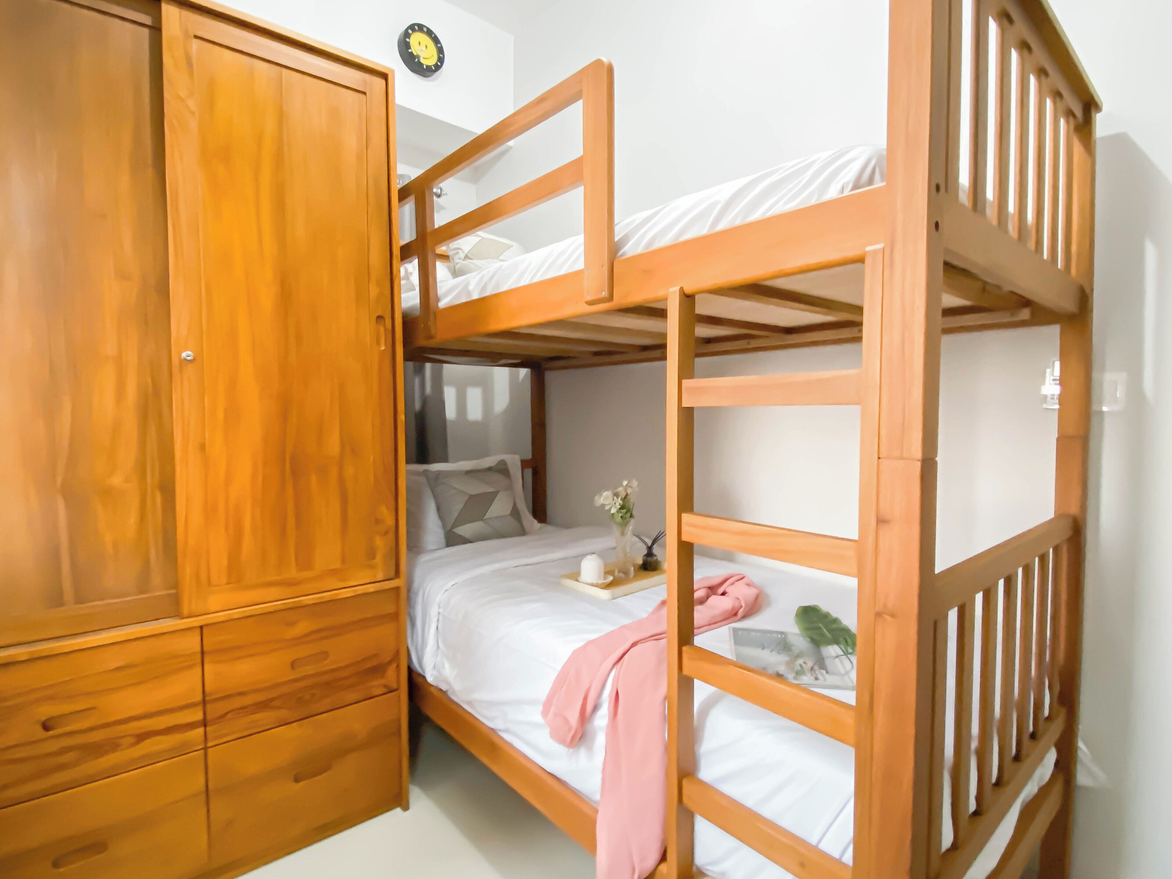 A bunk bed room with a wooden wardrobe and a clock on the wall.