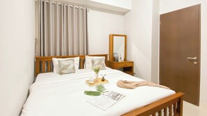 A neatly made bed with a wooden headboard, a bedside table with a mirror, and a door to the right. - Big And Cozy 3Br Apartment At Transpark Juanda Bekasi Timur (Bekasi)