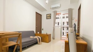 A living room with a sofa, a wooden table, a TV, and a window with curtains. - Big And Cozy 3Br Apartment At Transpark Juanda Bekasi Timur (Bekasi)