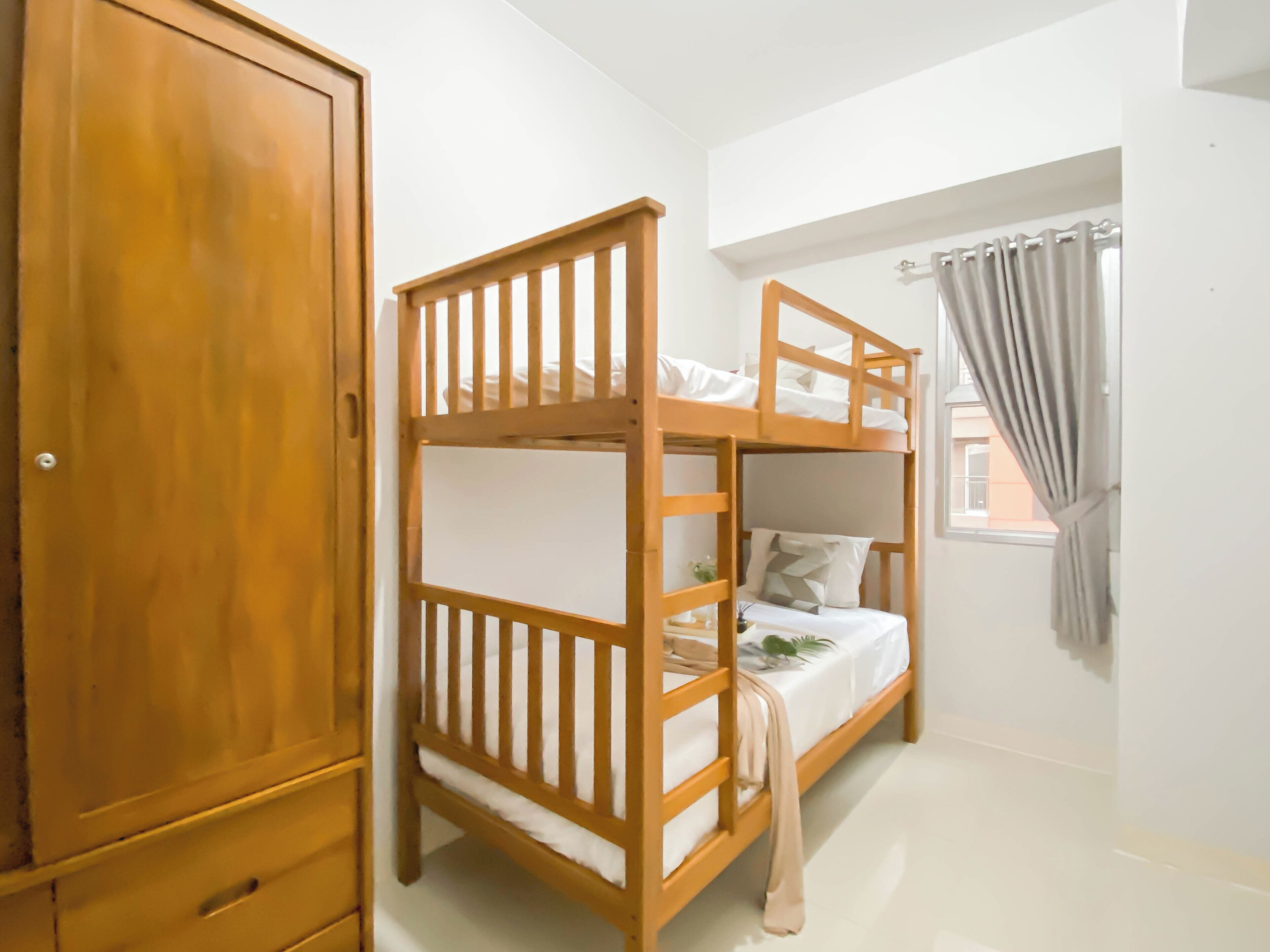 A bunk bed with a wooden frame, a wardrobe, and a window with curtains.
