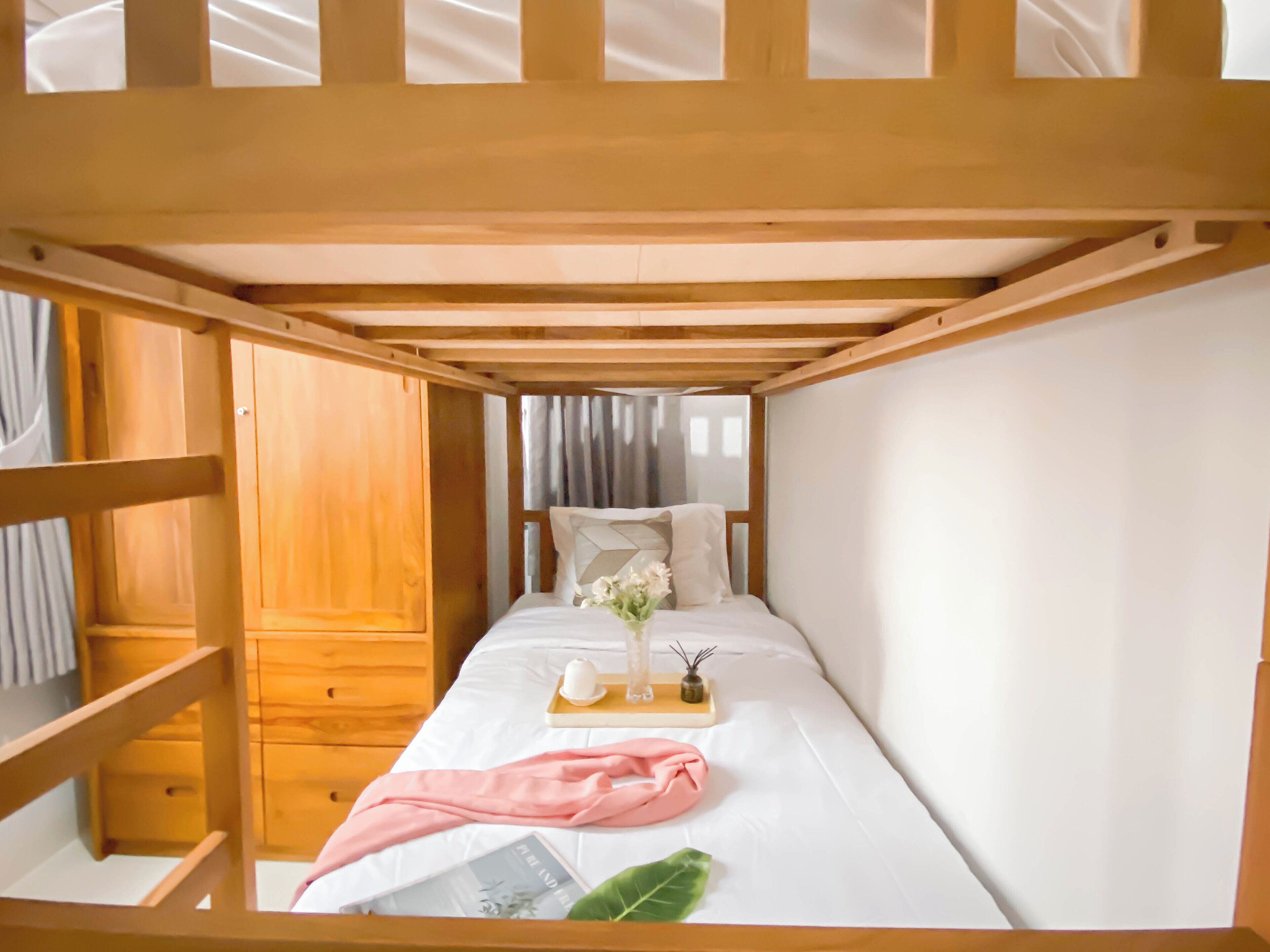 A single bed with a wooden headboard, a bedside table with a vase of flowers, a pink blanket, and a book.