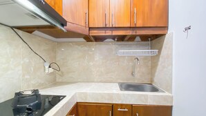 A kitchen with wooden cabinets, a stainless steel sink, and a black stove. - Big And Cozy 3Br Apartment At Transpark Juanda Bekasi Timur (Bekasi)