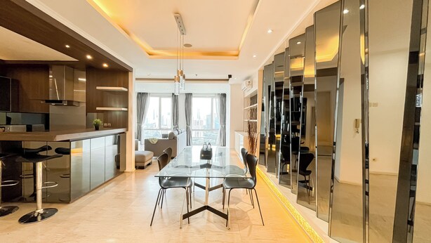 A modern kitchen with a central island, a dining area with a glass table, and a city view through large windows. - Spacious Luxury 2Br Apartment With Extra Room At Fx Residence (Jakarta)