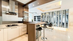 A modern kitchen with a gas stove, wooden cabinets, and a bar area with stools. - Spacious Luxury 2Br Apartment With Extra Room At Fx Residence (Jakarta)