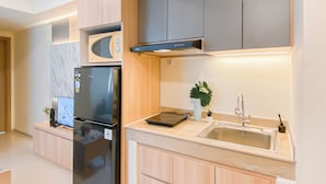 A modern kitchen with a built-in microwave, a stainless steel refrigerator, and a sink with a faucet. - Warm 2Br Apartment At Meikarta (Cikarang)
