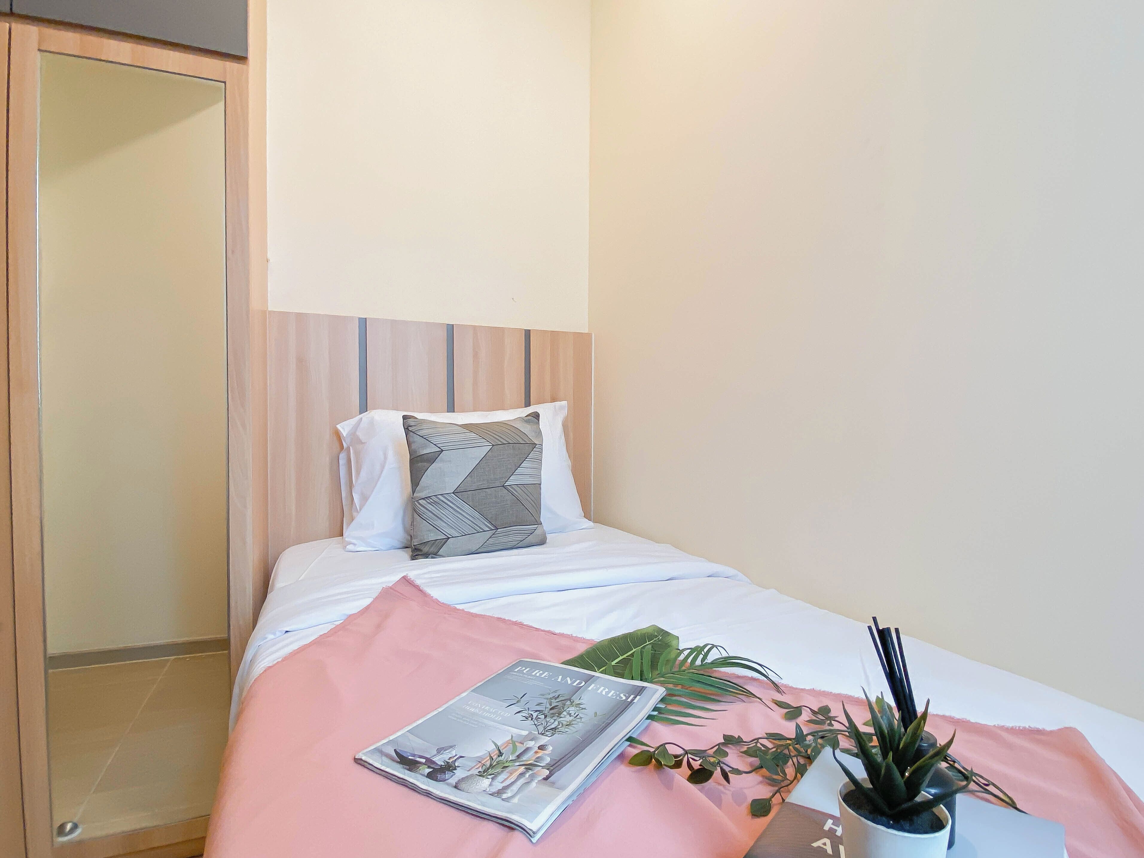Un letto ben rifatto con una rivista, una pianta e una coperta rosa.