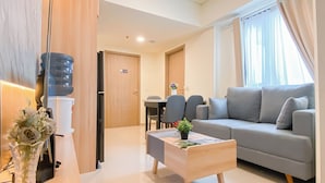 A modern living room with a grey sofa, a wooden coffee table, and a dining area with chairs and a table. - Warm 2Br Apartment At Meikarta (Cikarang)