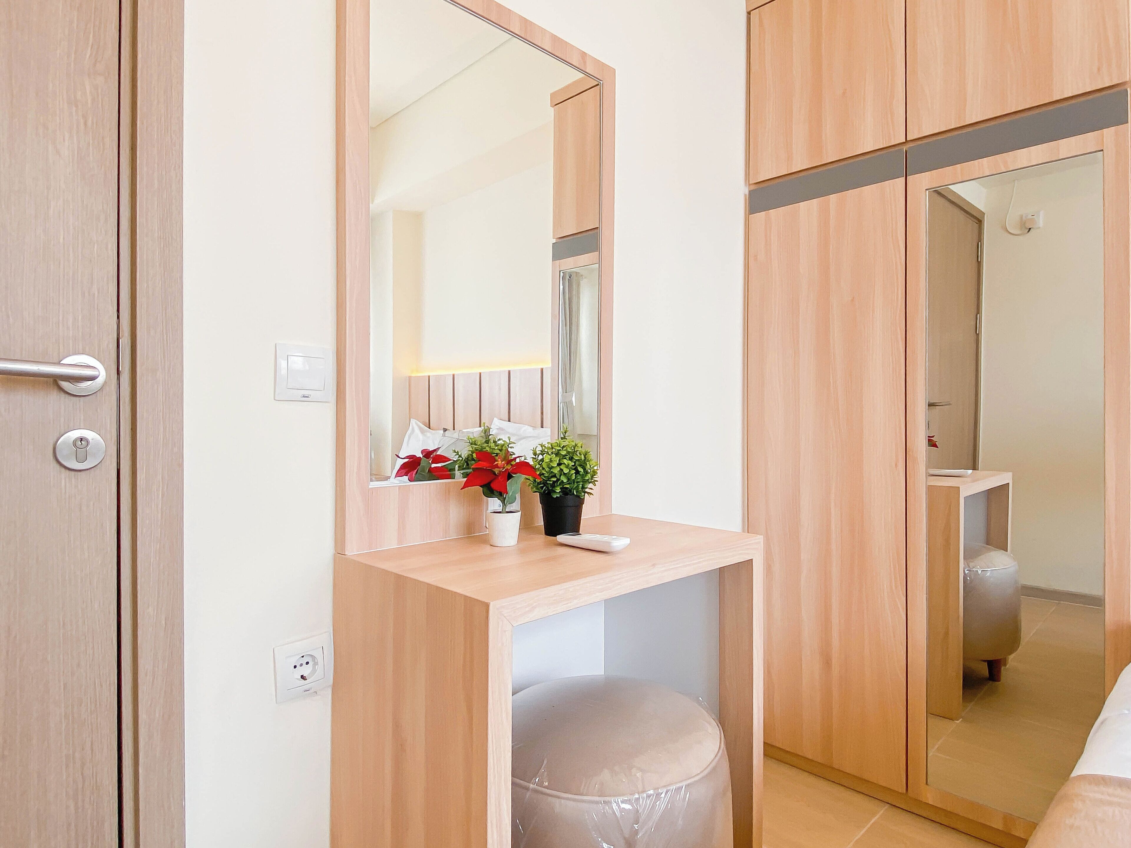 Une chambre d’hôtel avec une coiffeuse en bois, un miroir, une plante en pot et un petit tabouret.
