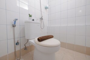 A bathroom with a white toilet, a shower head, and a towel on the toilet seat. - Soft Toned And Comfy 2Br Near Mall At Bassura City Apartment (Jakarta)