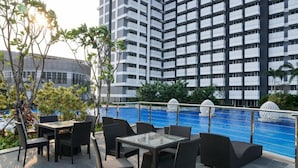 An outdoor seating area with tables and chairs, a pool, and a high-rise building in the background.