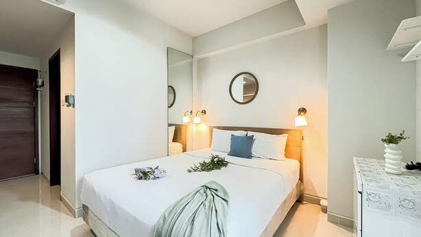 A hotel room with a large bed, a bedside table with a lamp, a mirror on the wall, and a door to the left.