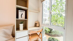 A neatly organized room with a bookshelf, a desk, a chair, and a window with a view of greenery and buildings. - Basic And Compact Studio At Tokyo Riverside Pik 2 Apartment (Teluknaga)