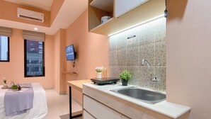 A modern hotel room with a kitchen area, including a sink, countertop, and a television mounted on the wall. - Peach Tone Studio At Evenciio Margonda Apartment (Depok)