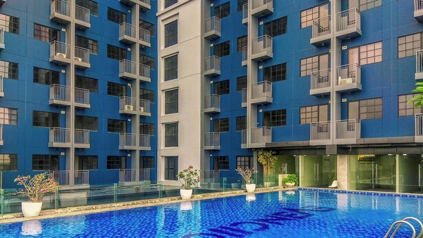 A swimming pool surrounded by a modern building with balconies. - Peach Tone Studio At Evenciio Margonda Apartment (Depok)