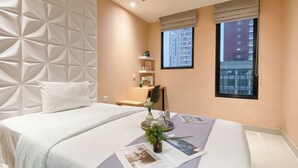 A modern hotel room with a large bed, a desk, a chair, and a window with a city view. - Peach Tone Studio At Evenciio Margonda Apartment (Depok)
