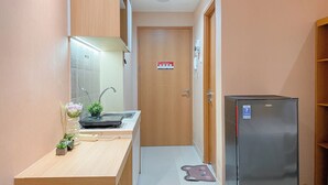 A narrow hallway with a wooden counter, a sink, and a refrigerator. - Peach Tone Studio At Evenciio Margonda Apartment (Depok)