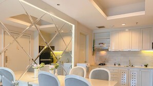 A modern kitchen with white cabinets, a central island, and a dining area with a glass partition. - Cozy Living 2Br Apartment Casa Grande Residence (Jakarta)