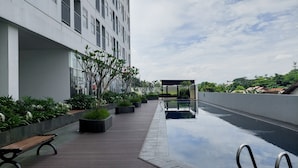 A modern outdoor pool area with a wooden deck, benches, and a clear sky. - Basic Studio Apartment Near Cisauk Station At Serpong Garden (Cisauk)