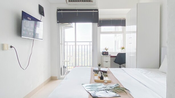 A hotel room with a bed, a desk, a chair, a TV, and a balcony with a view. - Basic Studio Apartment Near Cisauk Station At Serpong Garden (Cisauk)